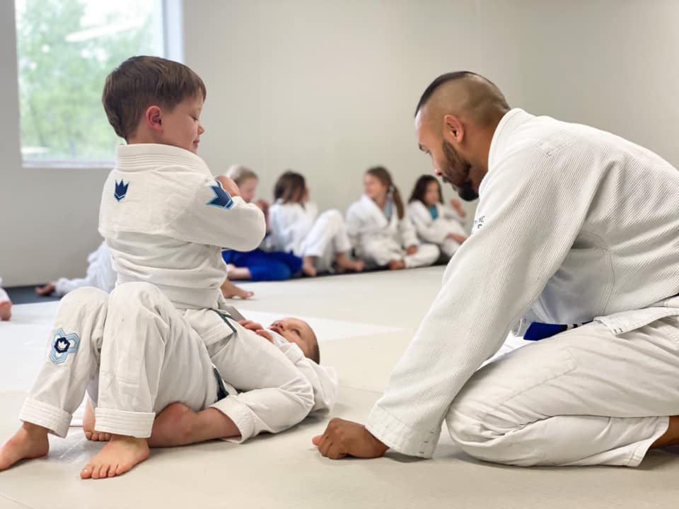 a coach at prodigy martial arts in blaine helps 2 kids doing jiu-jitsu
